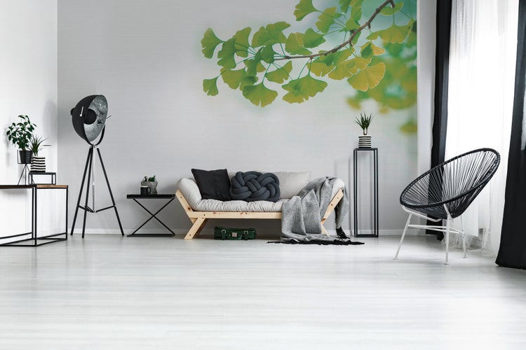 Modernes Wohnzimmer mit Fototapete eines Ginkgozweigs, hellem Holzsofa, schwarzer Dreibein-Stehlampe und einem Acapulco-Stuhl.
