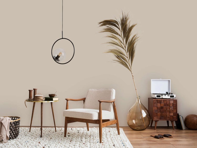 Modernes Wohnzimmer mit Sessel aus Holz, Ring-Pendelleuchte, großer Glasvase mit getrocknetem Palmwedel und hellem Teppich.