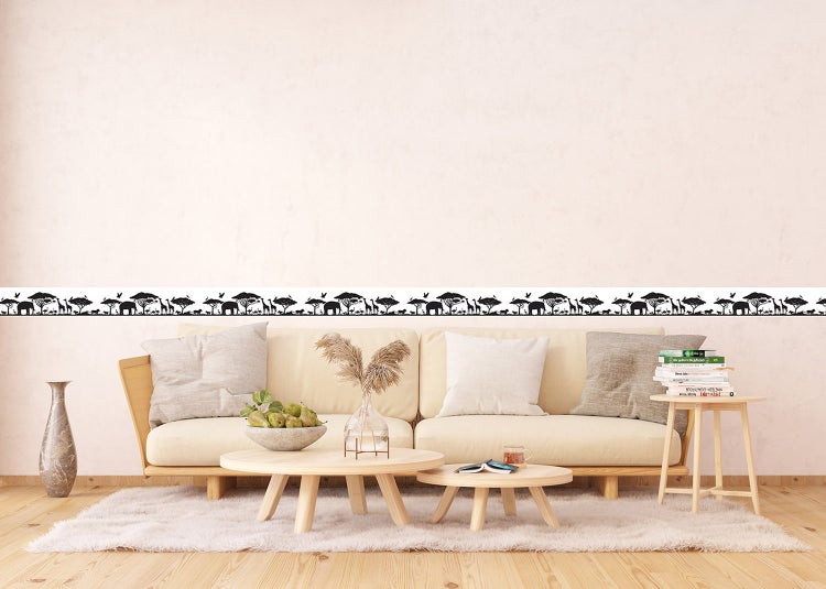 Selbstklebende Wandbordüre mit schwarzen afrikanischen Safari-Silhouetten in einem hellen Wohnzimmer über einem beigen Sofa.