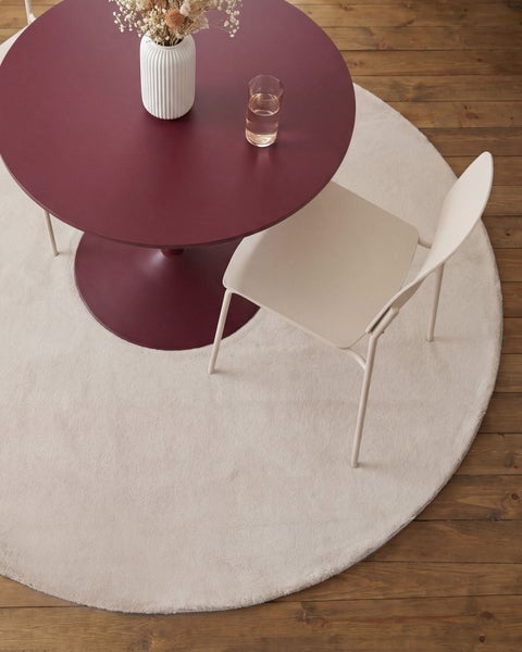 Moderner Essbereich mit rundem weinrotem Tisch, beigefarbenem Stuhl und passendem runden Teppich auf Holzboden.