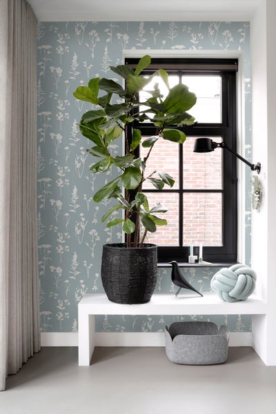 Helles Zimmer mit Feigenbaum im Korb, dekorativen Accessoires und floraler Tapete