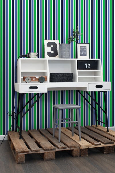 Weißer Schreibtisch mit Regalen und schwarzem Metallgestell vor einer gestreiften Tapete, mit einem grauen Hocker auf einer Holzpalette