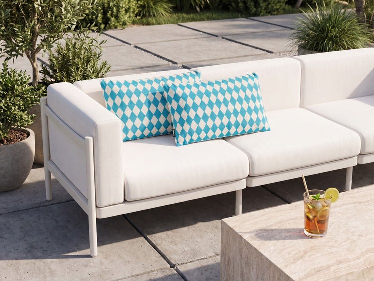 Modernes Loungesofa mit rautenförmigen Zierkissen auf einer Terrasse mit Steinfliesen und Beistelltisch.