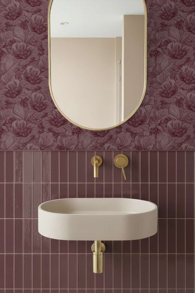 Modernes Badezimmer mit Waschtisch, ovalem Spiegel und Wandarmatur vor einer gefliesten Wand mit Blumensitz-Tapete.