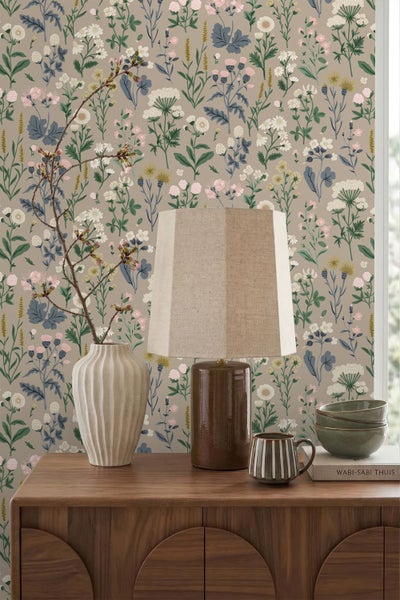 Vliestapete mit botanischem Wildblumen-Muster in einem Raum mit Sideboard aus Holz, Tischleuchte und Keramikvase.