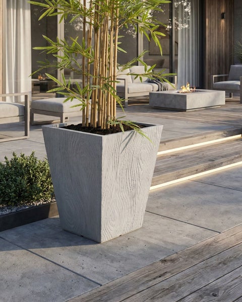 Szene mit einem quadratischen Pflanzgefäß aus Beton mit Bambuspflanze auf einer Terrasse.