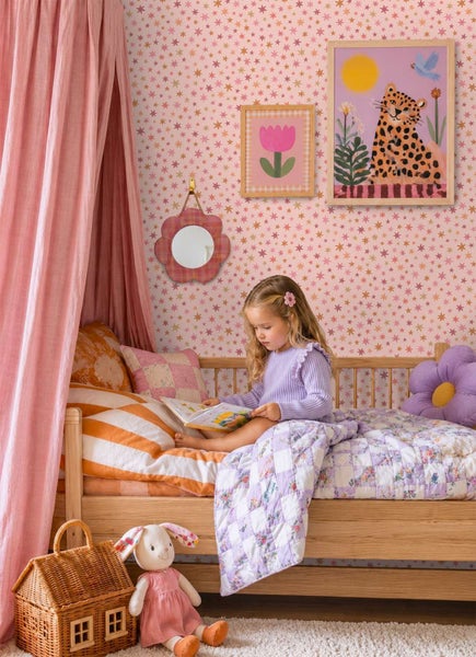 Ein Kinderzimmer mit Sternentapete, einem Holzbett mit Baldachin, einem karierten Patchwork-Quilt, Wandbildern und einem weichen Plüschtier.
