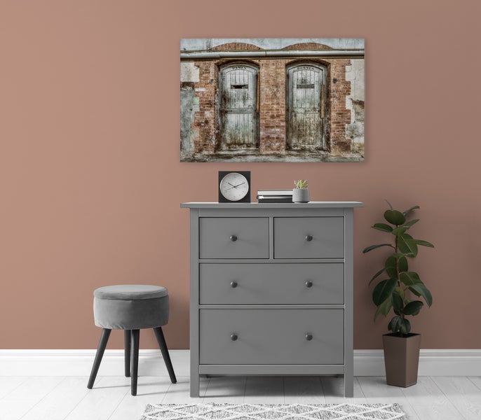 Wandbild mit Motiv von alten Holztüren in Ziegelwand über einer Kommode mit Hocker und Pflanze in einem modern eingerichteten Raum.