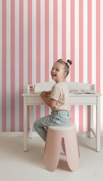 Mädchen sitzt am Schreibtisch vor einer gestreiften Tapete