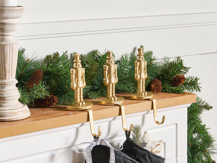 Dekoratives Weihnachtsszenario mit goldenen Nussknacker-Strumpfhaltern, Tannengirlande und Kerzenständer auf einem Kaminsims.