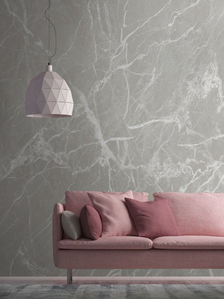 Rosa Sofa mit Kissen unter einer geometrischen Hängelampe vor einer Marmortapete