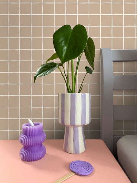 Dekorative Szene mit Kerze, Pflanze in gestreiftem Topf und Lolli auf einem Tisch