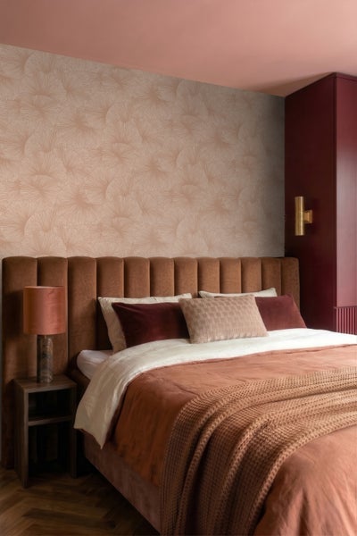 Vlies-Tapete mit Fächermuster im Schlafzimmer hinter gepolstertem Bett mit Kissen und Tischlampe.
