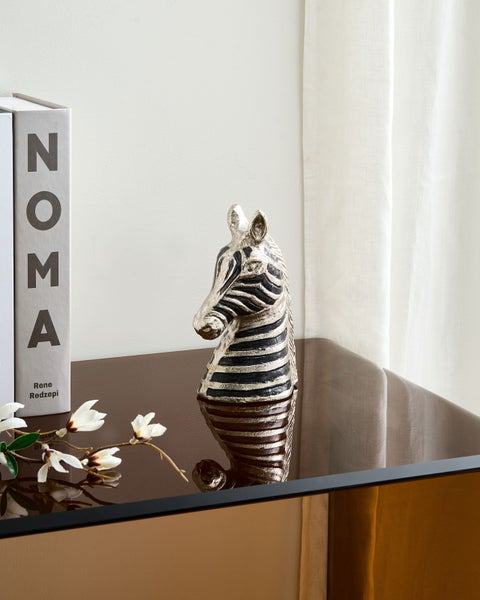 Dekorative Zebra-Skulptur auf einem Tisch mit Buch und Magnolienzweig