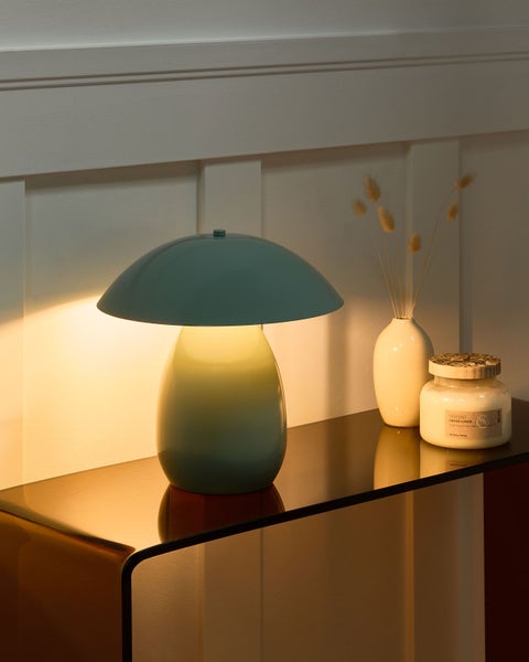 Pilzförmige Tischleuchte auf einer glänzenden Konsole neben einer Vase mit Trockenblumen und einer Duftkerze in warmem Licht.