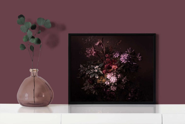 Wandbild mit Blumenstillleben in schwarzem Rahmen neben einer Glasvase mit Eukalyptuszweig auf einem Sideboard.