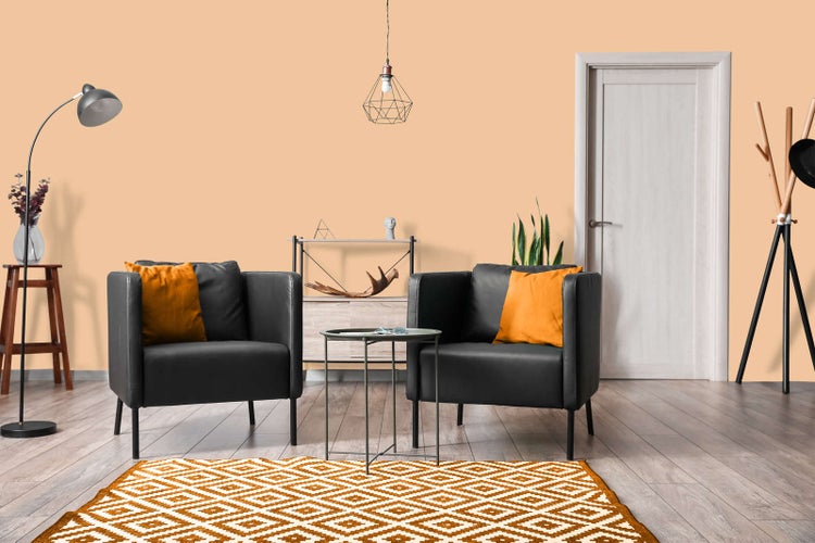 Modernes Wohnzimmer mit orangefarbener Wand, zwei schwarzen Sesseln mit orangefarbenen Kissen, gemustertem Teppich und Holzboden.