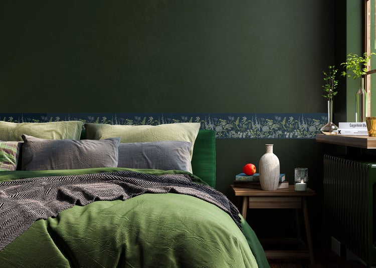 Tapetenbordüre mit Wiesenblumenmuster an einer dunkelgrünen Wand in einem Schlafzimmer über einem Bett.