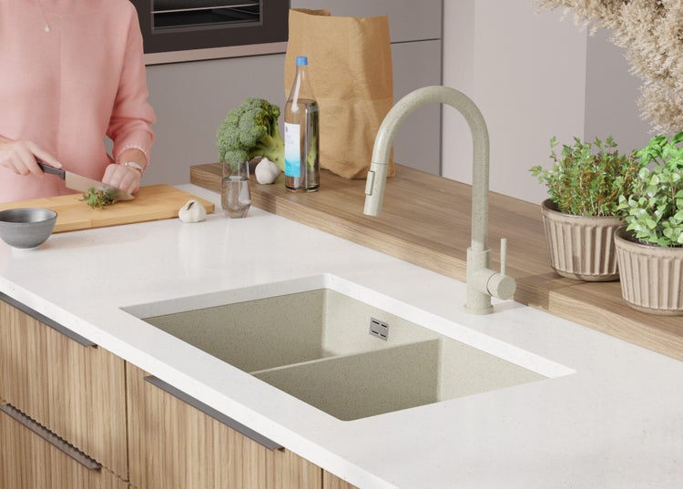 Küchenszene mit Doppelspüle, Armatur und Person, die Gemüse schneidet