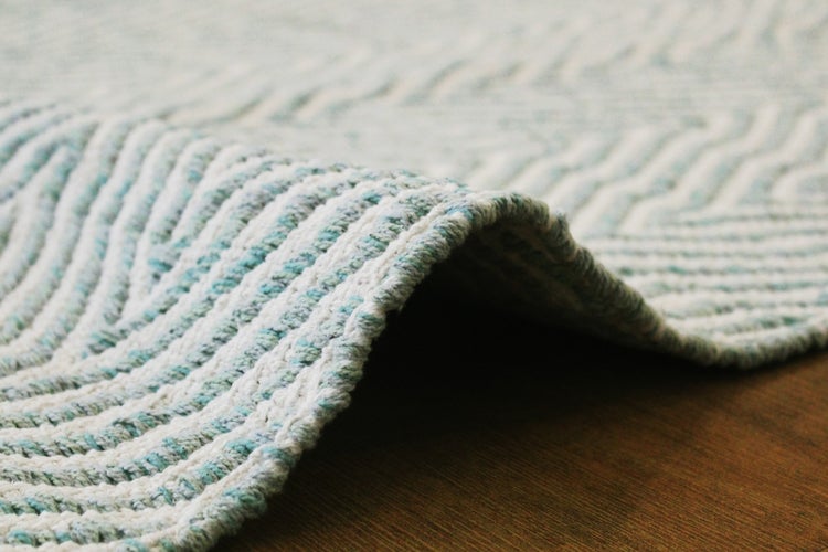 Detailaufnahme eines gewebten Teppichs mit Chevron-Muster auf einem Holzboden.