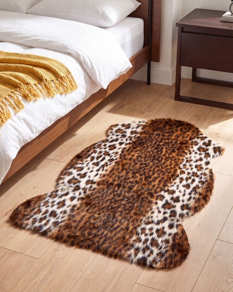 Kunstfell Teppich mit Leopardenmuster vor einem Bett in einem Schlafzimmer mit Holzboden