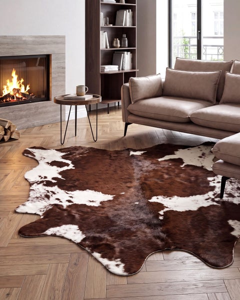 Wohnzimmer mit Kuhfellteppich, Ledersofa, Kamin und Holzregal auf Parkettboden in einem modernen Wohnbereich.