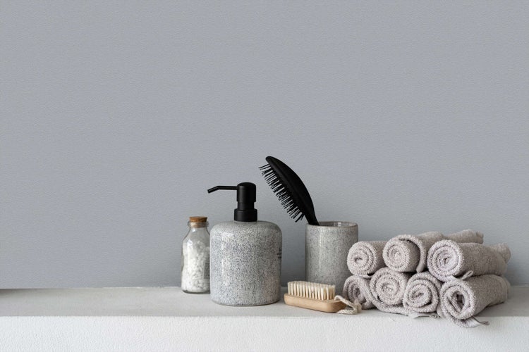 Modernes und organisiertes Badezimmer mit Seifenspender, Becher, Haarbürste und gerollten Handtüchern vor einer strukturierten Wand.