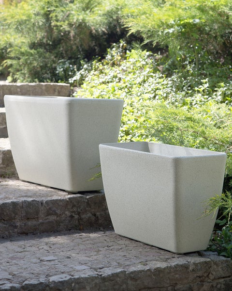 Zwei rechteckige Pflanzkübel aus Stein auf einer Steintreppe im Garten.