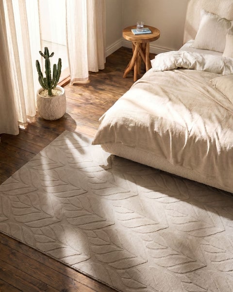 Beiger Teppich mit geprägtem Blattmuster in einem hellen Schlafzimmer mit Holzfußboden, Bett und einem Kaktus.