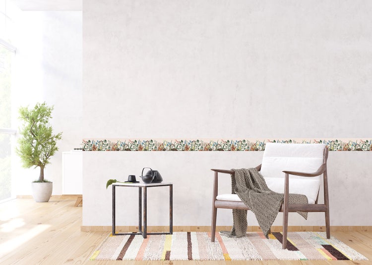 Hell gestalteter Wohnraum mit einer Blumen-Tapetenbordüre an der Wand, Sessel, Beistelltisch und gemustertem Teppich auf Holzfußboden.