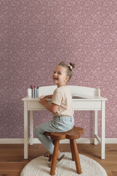 Mädchen sitzt an einem Schreibtisch vor einer Wand mit Blumentapete.