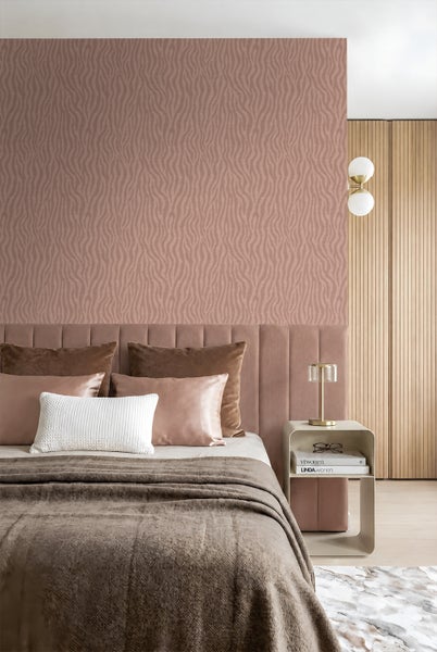 Schlafzimmer mit gemusterter Tapete mit Wellenlinien hinter einem gepolsterten Kopfteil und einem Nachttisch mit Tischleuchte.