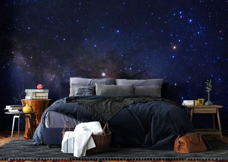 Fototapete mit Galaxie-Motiv in einem modern eingerichteten Schlafzimmer mit dunklem Bett und Nachttischen aus Holz.