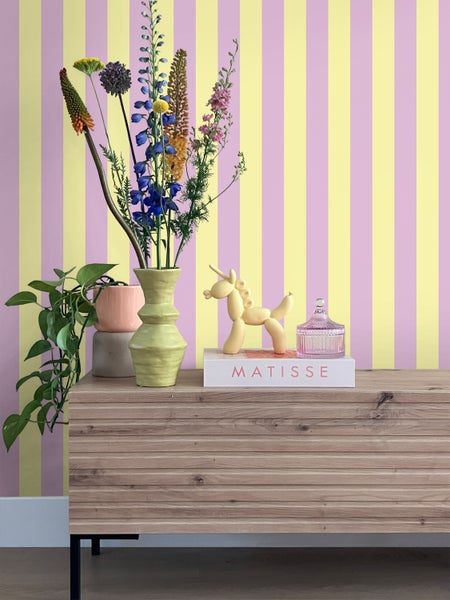 Dekoratives Stillleben mit Blumenstrauß, Ziergefäßen und Accessoires auf einem Holzschrank vor gestreifter Tapete