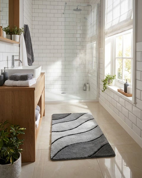Modernes, helles Badezimmer mit grauem Badteppich mit Wellenmuster, Holzwaschtisch mit weißem Waschbecken, begehbarer Dusche und weißen Fliesen.