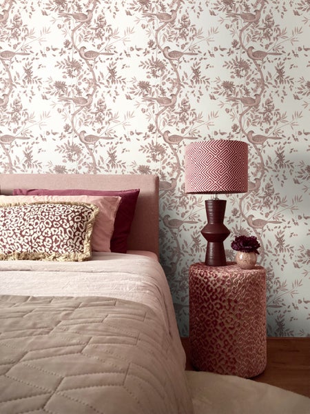 Vliestapete mit Vogel- und Blumenmuster im Chinoiserie-Stil in einem gemütlich eingerichteten Schlafzimmer mit gemusterten Kissen.