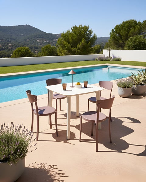 Szene mit einem weißen Gartentisch und vier Stühlen auf einer Terrasse am Pool.