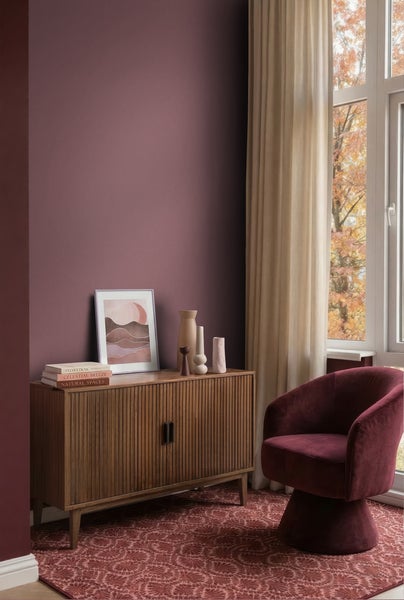 Modernes Wohnzimmer mit matter Wandfarbe, Sideboard aus Holz, Samtsessel und gemustertem Teppich vor einem Fenster.