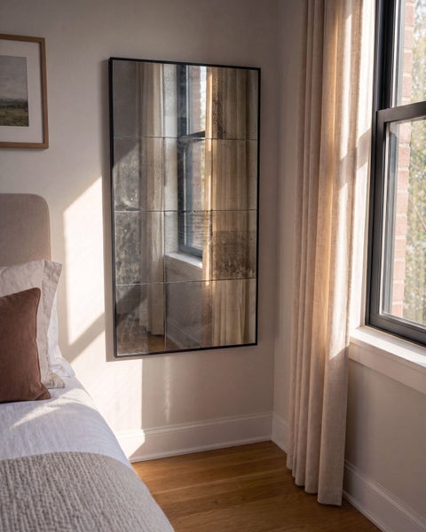 Rechteckiger Wandspiegel mit schwarzem Metallrahmen und antikem Spiegelglas im Kachel-Design in einem hellen Schlafzimmer.