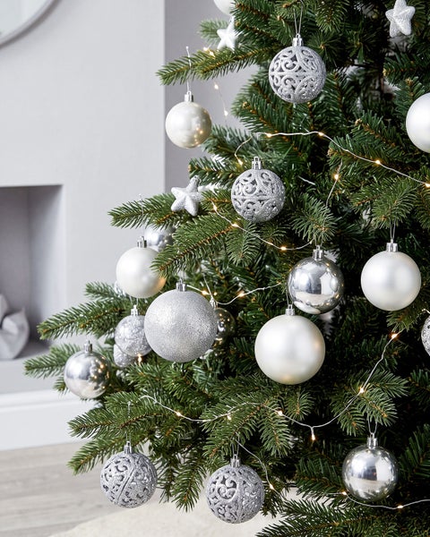 Geschmückter Weihnachtsbaum mit glänzenden und matten Christbaumkugeln und einer Lichterkette in einem weihnachtlich dekorierten Raum