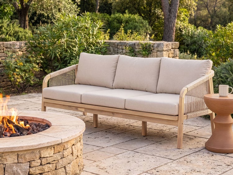 3-Sitzer Gartensofa aus Holz mit Seilbespannung und Polstern neben einer gemauerten Feuerstelle auf einer Steinterrasse.