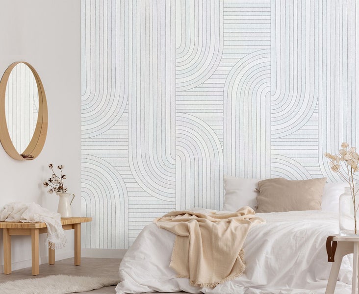 Helles Schlafzimmer mit Bett, Spiegel und Wandtapete mit geometrischem Muster.