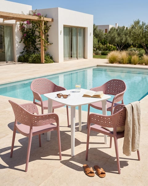 Gartenmöbel-Set mit weißem quadratischem Tisch und vier mauvefarbenen Stühlen mit Lochmuster an einem Pool auf einer hellen Terrasse.