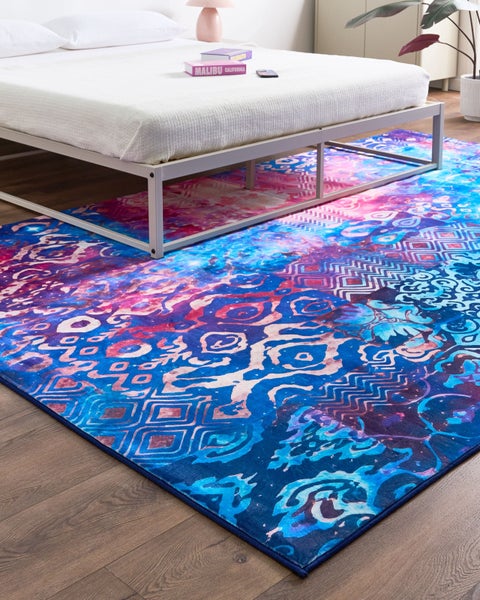 Moderner Teppich mit buntem Ethno-Muster unter einem Metallbettrahmen in einem hellen Schlafzimmer auf Holzboden.