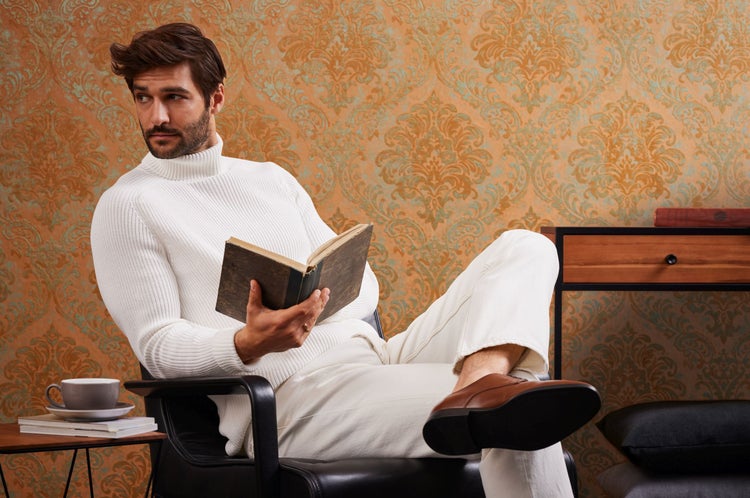 Mann vor einer Wand mit floralem Muster, bekleidet mit einem braunen karierten Hemd