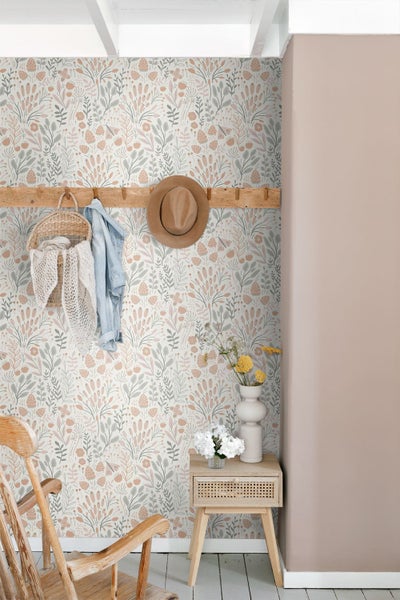 Vliestapete mit botanischem Muster in Pastelltönen in einem hellen Raum mit Holzmöbeln und Wandgarderobe.