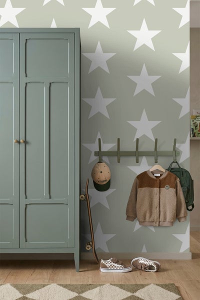 Tapete mit großen weißen Sternen im Kinderzimmer neben einem grünen Kleiderschrank, Garderobenleiste mit Kleidung und einem Skateboard.