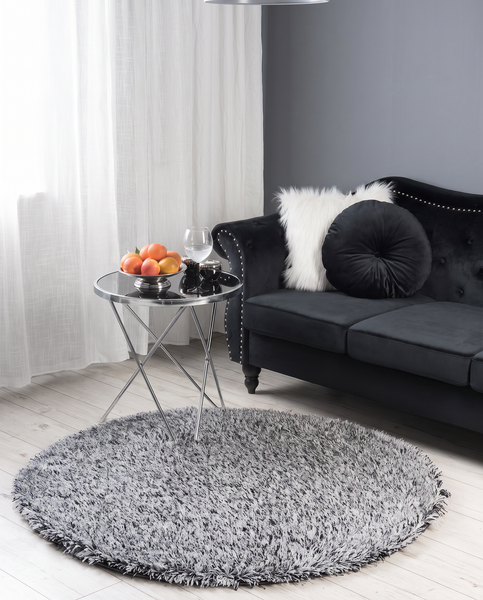 Wohnzimmer mit dunklem Samtsofa, rundem Beistelltisch aus Glas und Metall sowie einem runden, grauen Hochflor-Teppich auf hellem Holzboden.