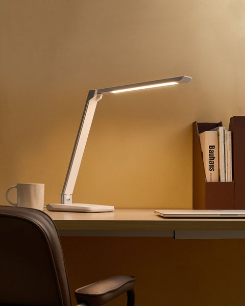 Szene mit Schreibtischlampe, Tasse, Laptop und Buchmagazin auf einem Schreibtisch