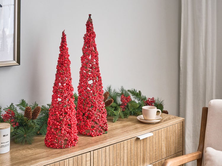Dekorative Weihnachtstannen aus roten Beeren und Tannengirlande auf einem Sideboard